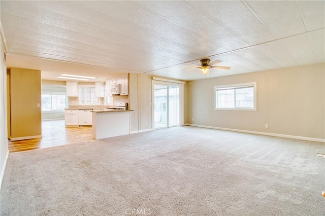 unfurnished living room featuring ceiling fan, light carpet, and a wealth of natural light