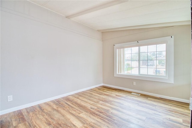 empty room featuring beamed ceiling and light hardwood / wood-style flooring