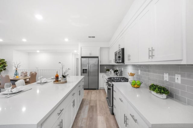 kitchen featuring a kitchen island, stainless steel appliances, light hardwood / wood-style floors, decorative backsplash, and white cabinets