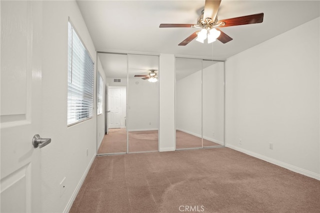 unfurnished bedroom featuring multiple closets, light colored carpet, baseboards, and a ceiling fan