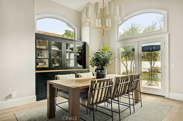 dining room with a high ceiling, a wealth of natural light, a notable chandelier, and light hardwood / wood-style floors