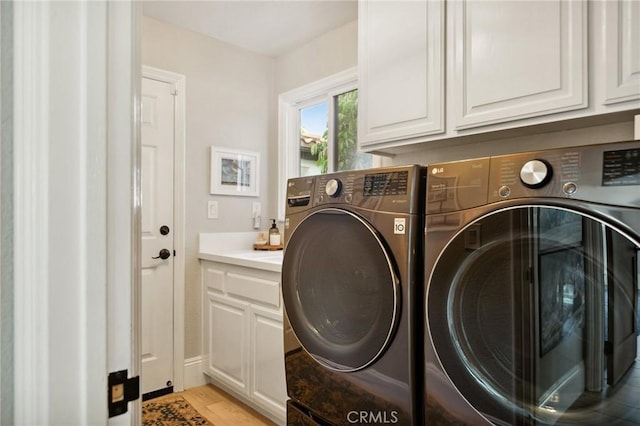 laundry room featuring cabinets, washing machine and clothes dryer, and light wood-type flooring