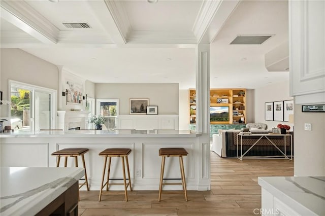 kitchen featuring a wealth of natural light, light stone countertops, white cabinets, and a kitchen bar