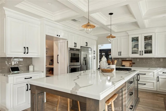 kitchen featuring a breakfast bar, stainless steel appliances, a center island, light stone countertops, and white cabinets