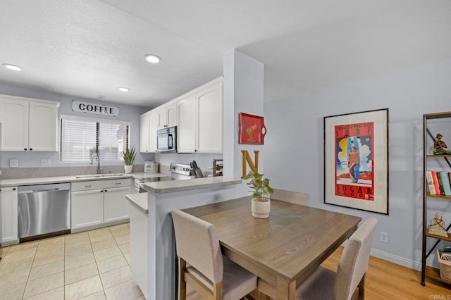 kitchen with sink, light tile patterned floors, white cabinetry, stainless steel appliances, and kitchen peninsula