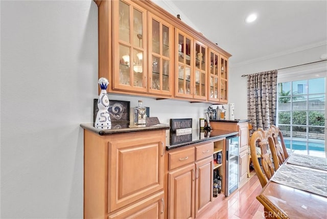 bar with crown molding, wine cooler, dark stone counters, and light hardwood / wood-style flooring