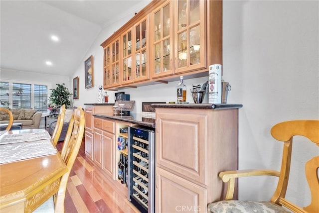 bar featuring lofted ceiling, light hardwood / wood-style flooring, beverage cooler, and dark stone counters