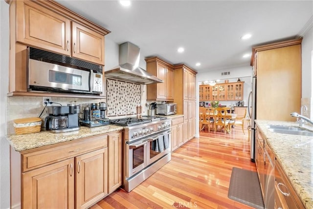 kitchen featuring sink, light stone counters, stainless steel appliances, light wood-type flooring, and wall chimney exhaust hood