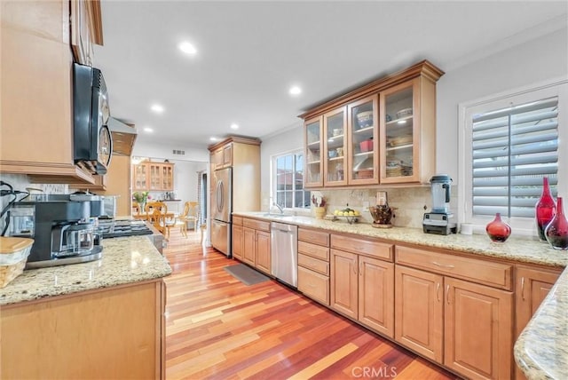 kitchen featuring light stone counters, backsplash, stainless steel appliances, and light wood-type flooring