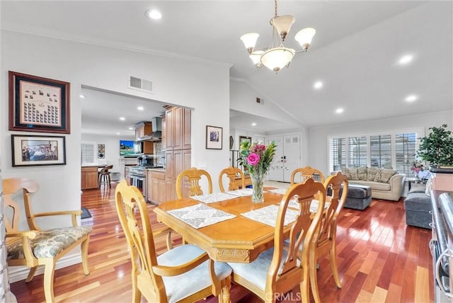 dining area with a notable chandelier, ornamental molding, vaulted ceiling, and light wood-type flooring