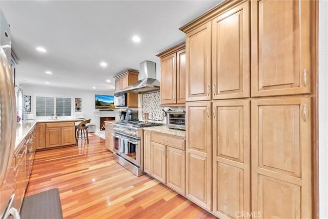 kitchen featuring decorative backsplash, double oven range, light hardwood / wood-style floors, light stone countertops, and wall chimney exhaust hood