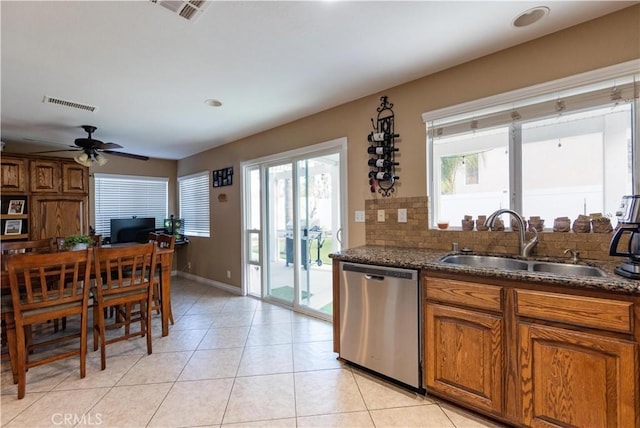 kitchen featuring sink, dark stone countertops, light tile patterned floors, stainless steel dishwasher, and decorative backsplash