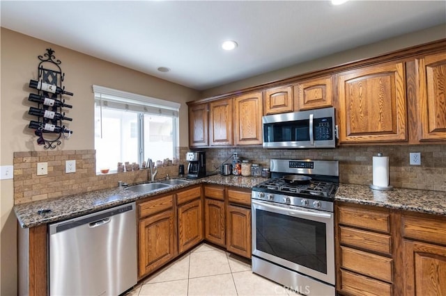 kitchen with light tile patterned floors, stainless steel appliances, sink, and dark stone countertops