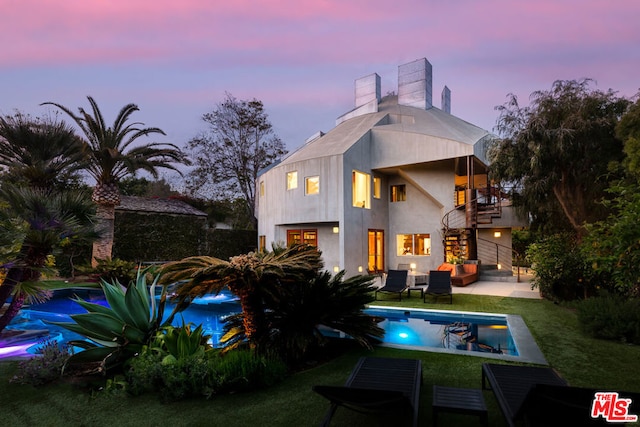 back house at dusk with a yard and a balcony