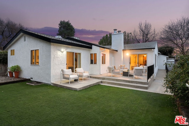 back house at dusk featuring a yard, a patio, and an outdoor living space with a fire pit