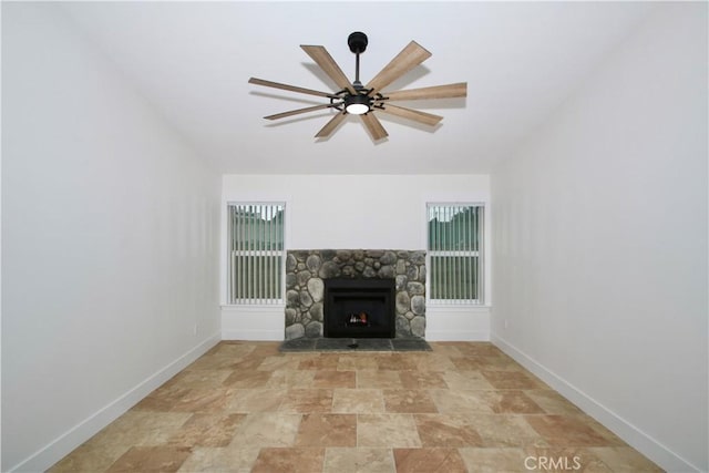 unfurnished living room with a stone fireplace and ceiling fan