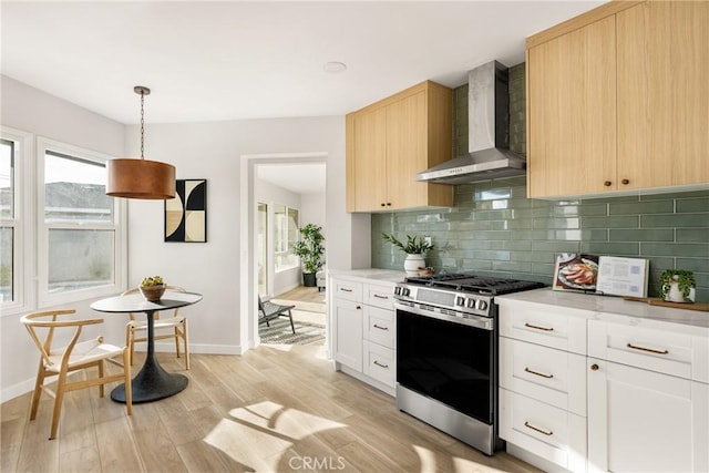 kitchen with hanging light fixtures, light brown cabinetry, white cabinetry, wall chimney range hood, and stainless steel gas range