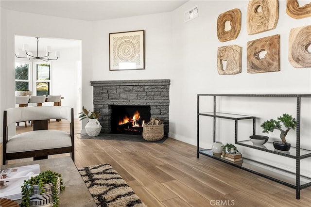 living room featuring a notable chandelier, a fireplace, wood finished floors, visible vents, and baseboards