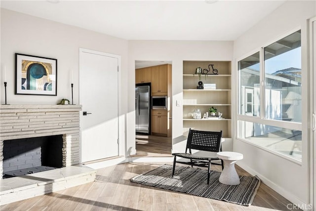 sitting room featuring baseboards, wood finished floors, and a stone fireplace