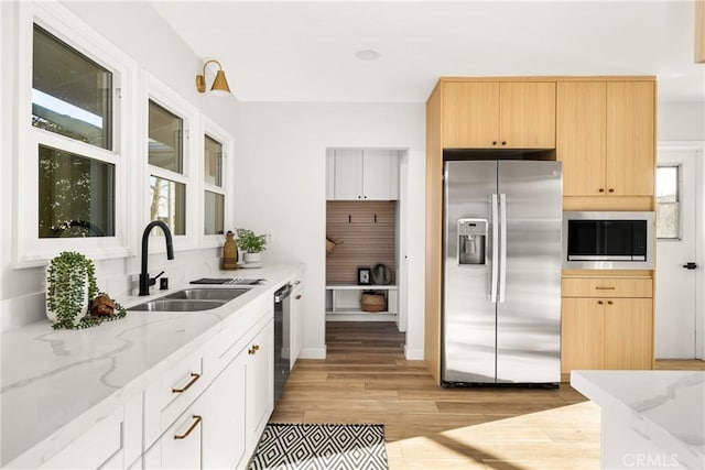 kitchen with light brown cabinetry, stainless steel refrigerator with ice dispenser, a sink, and light stone countertops