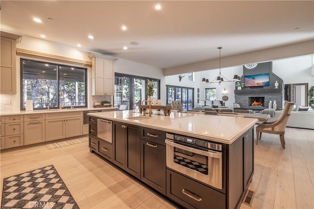 kitchen featuring light countertops, backsplash, light wood-style floors, open floor plan, and a warm lit fireplace