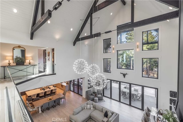 living area with high vaulted ceiling, a notable chandelier, beamed ceiling, and wood finished floors