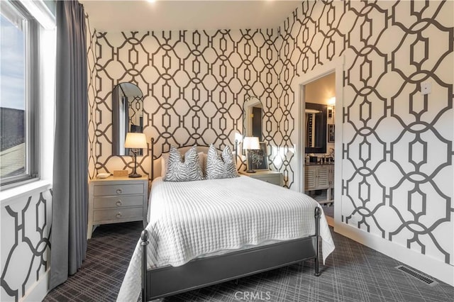 bedroom with wallpapered walls, visible vents, dark carpet, and ensuite bathroom