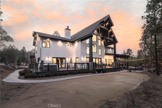 back of property at dusk featuring stairs, a chimney, and stucco siding