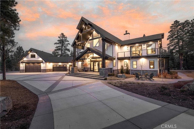 view of front of house with an attached garage, a balcony, stone siding, concrete driveway, and stucco siding