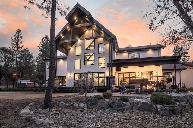 back of house at dusk with a patio, an outdoor fire pit, and stucco siding