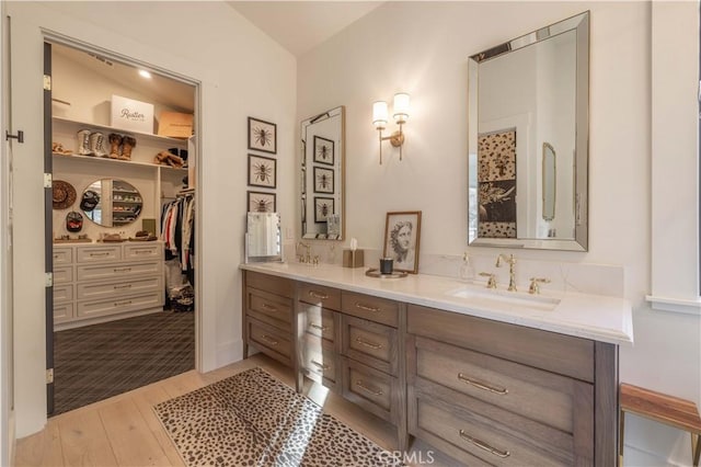 full bath with double vanity, wood finished floors, a sink, and a walk in closet