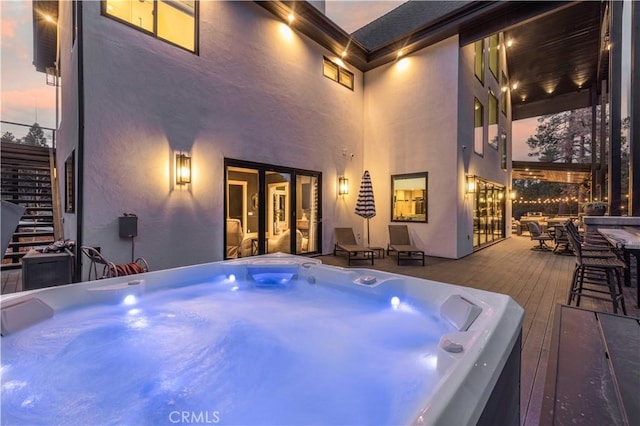 deck at dusk featuring hot tub deck surround, stairs, and outdoor dining area