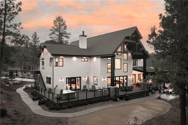 back of property at dusk featuring stairs, a patio, a chimney, and stucco siding