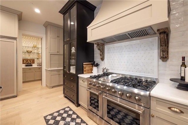 kitchen with high end appliances, light wood-style flooring, light countertops, premium range hood, and recessed lighting