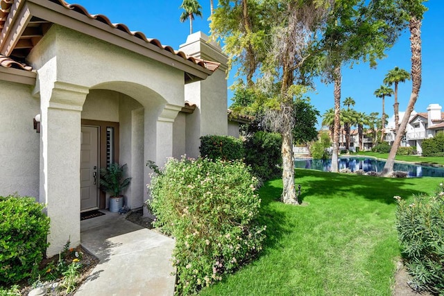 view of exterior entry featuring a water view and a lawn