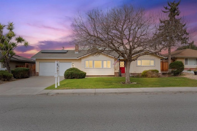 ranch-style house with a garage, a yard, and solar panels