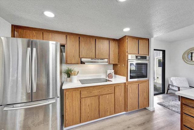 kitchen with stainless steel appliances, a textured ceiling, and light wood-type flooring