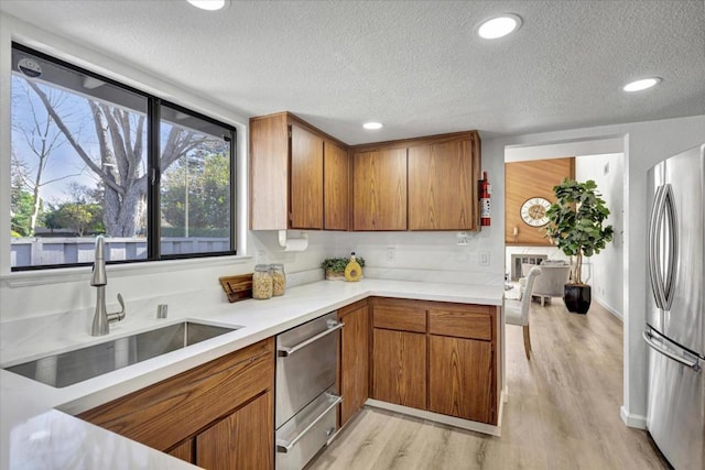 kitchen with sink, a textured ceiling, stainless steel refrigerator, and light hardwood / wood-style flooring