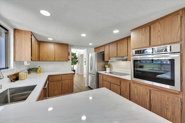 kitchen featuring sink, stainless steel appliances, light hardwood / wood-style floors, and a textured ceiling