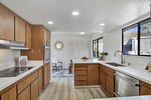 kitchen with sink, kitchen peninsula, stainless steel appliances, a textured ceiling, and light hardwood / wood-style flooring