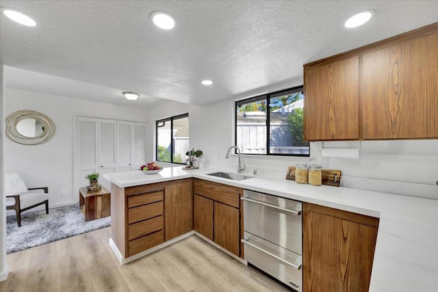 kitchen with sink, light hardwood / wood-style flooring, a textured ceiling, and kitchen peninsula