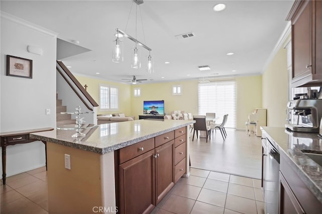 kitchen featuring light tile patterned flooring, ornamental molding, an island with sink, and hanging light fixtures