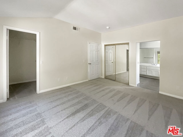 unfurnished bedroom featuring ensuite bath, lofted ceiling, carpet flooring, and a closet