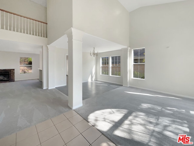 unfurnished living room featuring ornate columns, high vaulted ceiling, light carpet, and an inviting chandelier