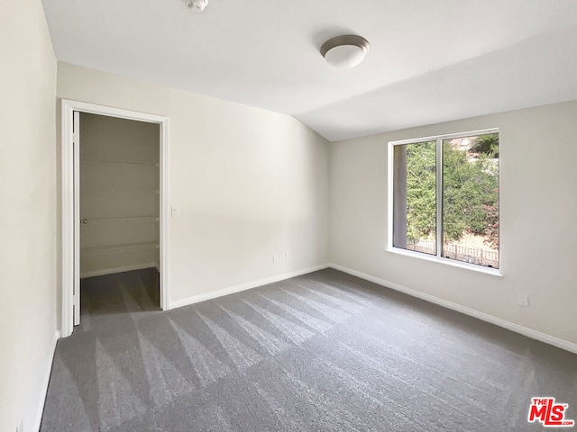 unfurnished bedroom with a walk in closet, lofted ceiling, and dark carpet