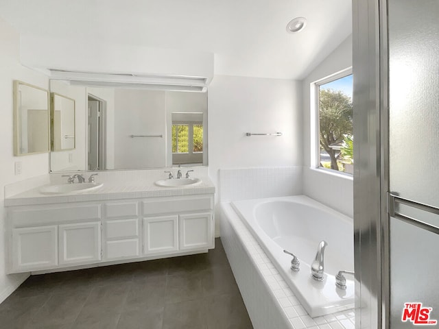 bathroom with a relaxing tiled tub, vanity, vaulted ceiling, and tile patterned floors