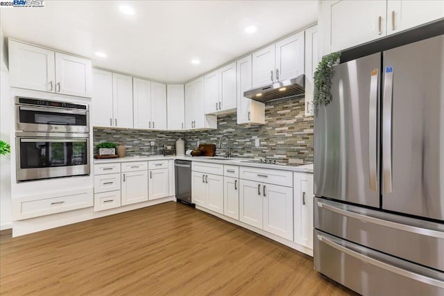 kitchen with sink, white cabinetry, appliances with stainless steel finishes, light hardwood / wood-style floors, and backsplash