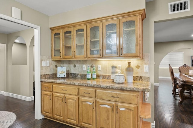 bar with tasteful backsplash, dark wood-type flooring, and light stone countertops