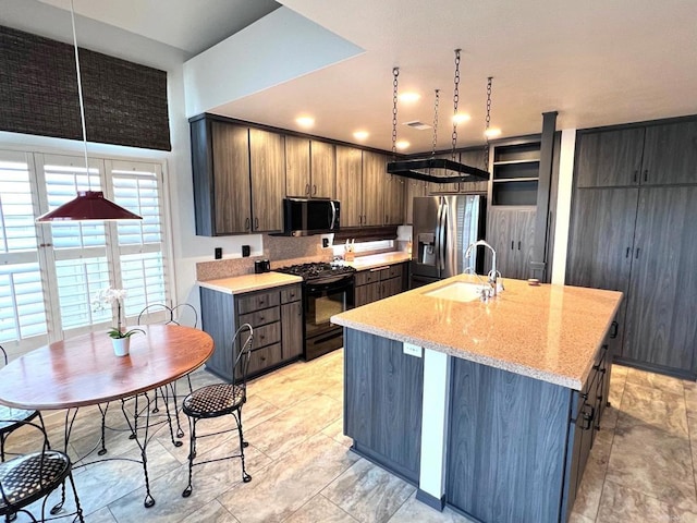 kitchen with sink, stainless steel appliances, light stone counters, dark brown cabinetry, and a center island with sink