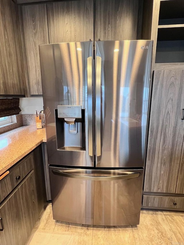 kitchen featuring light tile patterned flooring, stainless steel fridge, light stone countertops, and dark brown cabinets